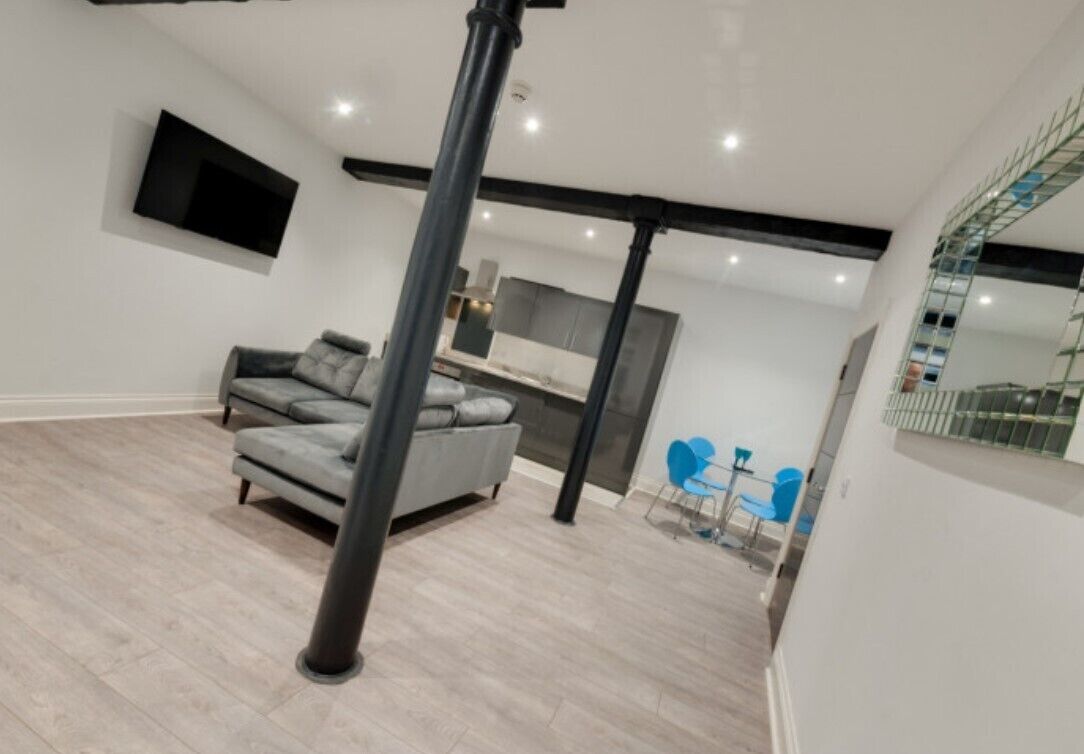 A modern living room with a grey sofa, a TV mounted on the wall, and a staircase leading to an upper level.
