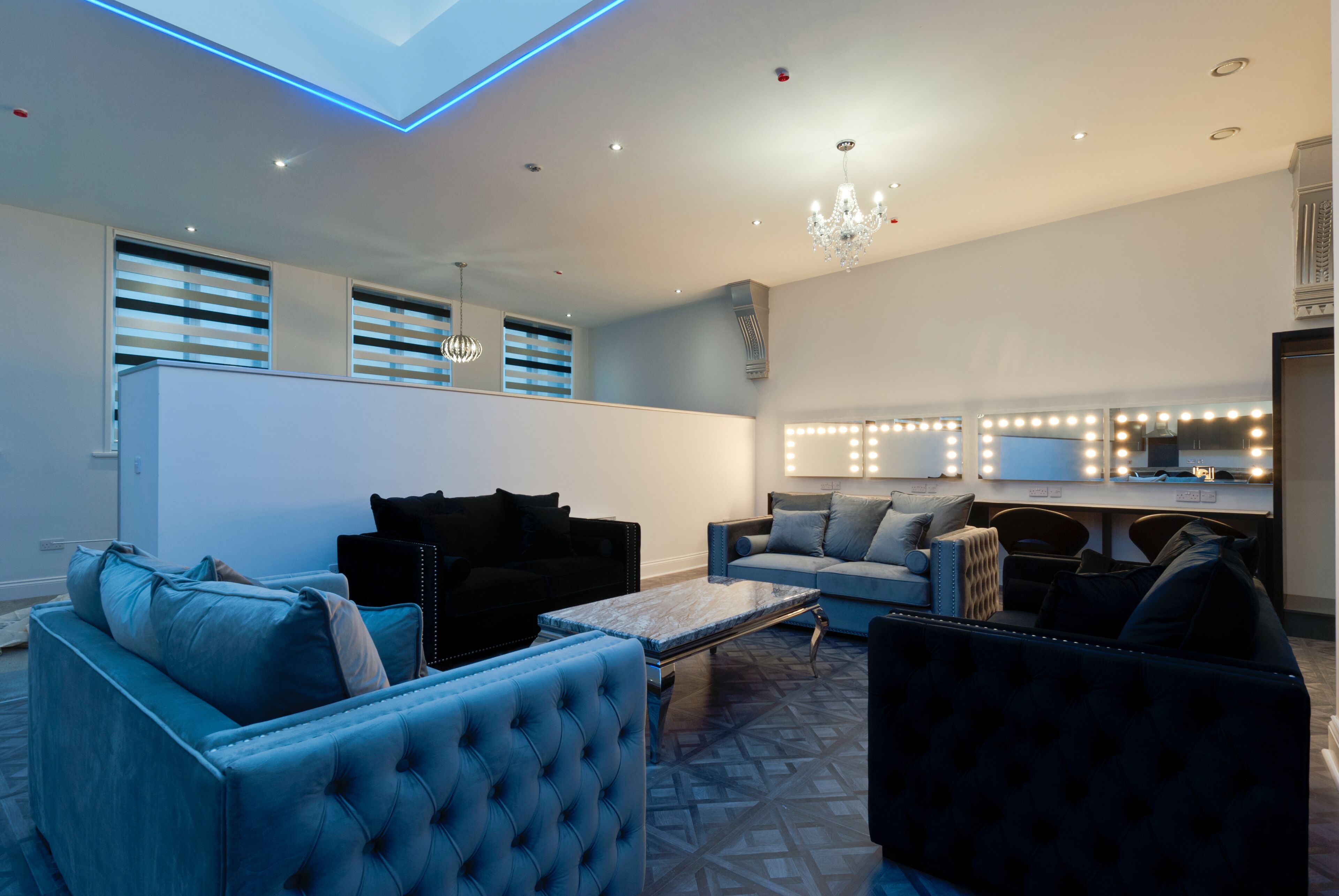 A modern living room with a sofa, armchairs, and a coffee table. There is a chandelier and a vanity with lights.