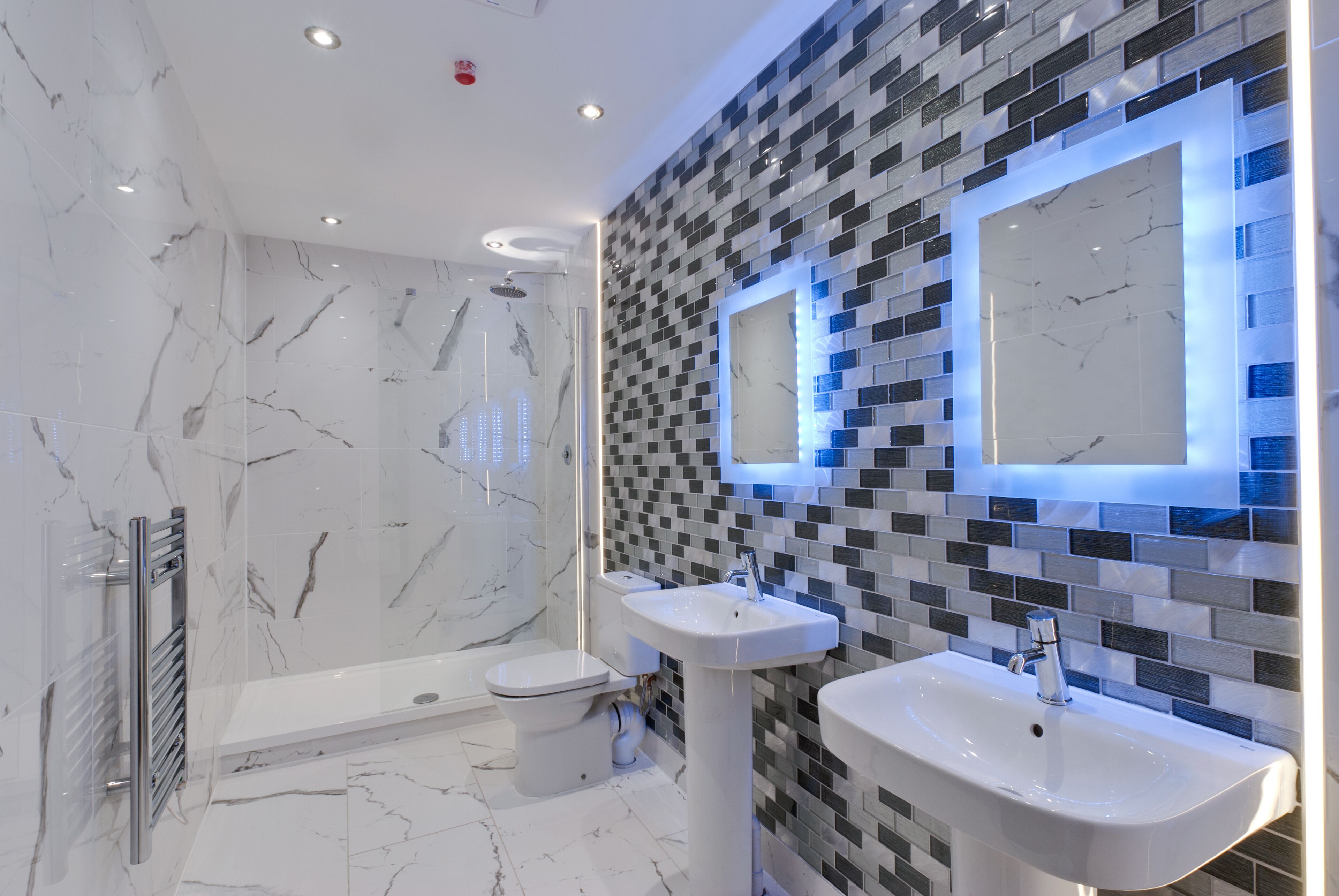 A modern bathroom with a marble floor, a shower, two sinks, and a toilet.