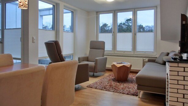 Ein modernes Wohnzimmer mit Essbereich, großen Fenstern und einem Kamin.