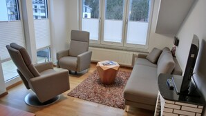 Ein modernes Wohnzimmer mit einer Couch, zwei Sesseln, einem Couchtisch und einem Fernseher.