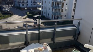 Ein Balkon mit Tisch für zwei Personen, Stühlen und Blick auf Gebäude im Hintergrund.