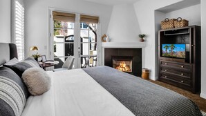 Un dormitorio con una cama grande, chimenea, televisor y balcón con vistas.