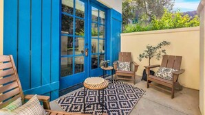Un patio con una puerta azul, sillas de madera, una mesita redonda y una alfombra estampada.