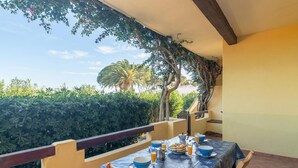 A balcony with a table set for breakfast, surrounded by greenery and a clear sky. - Piazzetta Trilo Porto 30m From The Beach (Loiri Porto San Paolo)