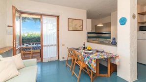 A dining area with a table set for four, a sofa, and a view through a glass door to an outdoor patio. - Piazzetta Trilo Porto 30m From The Beach (Loiri Porto San Paolo)