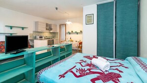 Ein Zimmer mit einem Bett, einem Schreibtisch mit Fernseher, einer Küchenzeile und einem Essbereich.