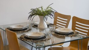 Une table à manger dressée avec des assiettes, des verres et un vase contenant une plante.
