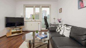 Un salon moderne doté d’un téléviseur à écran plat, d’une table basse en verre, d’un canapé en cuir noir et offrant une vue sur la ville grâce à de grandes fenêtres.
