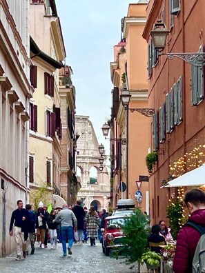A narrow street with historic buildings, cobblestone pavement, and a prominent archway in the distance. - Lussuoso appartamento vicino al Colosseo (Rome)