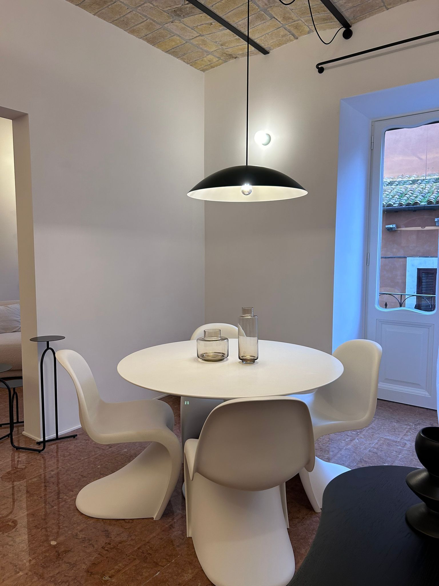 A modern dining area with a round table, white chairs, and a black pendant light.