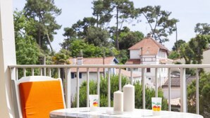 A balcony with a white railing, a white table, a white chair with an orange cushion, and two candles. - Studio 70, Centre, Proche des Plages (Saint-Palais-sur-Mer)