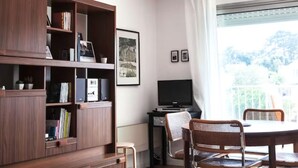 A room with a wooden bookshelf, a television, a dining table with chairs, and a window with curtains. - Studio 70, Centre, Proche des Plages (Saint-Palais-sur-Mer)