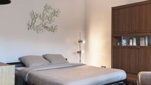 A bedroom with a bed, a wall-mounted lamp, and a wooden wardrobe. - Studio 70, Centre, Proche des Plages (Saint-Palais-sur-Mer)
