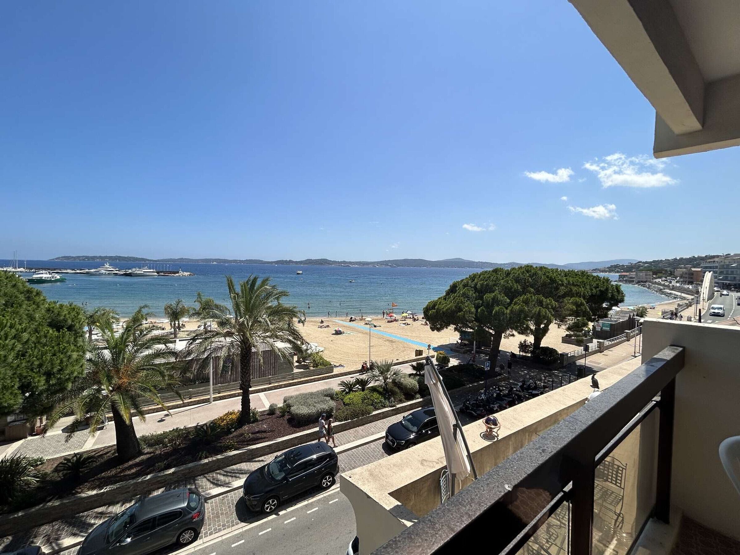 Ein Balkon mit Blick auf einen Strand, geparkte Autos und einen klaren Himmel.