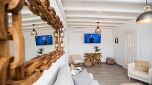 A modern living room with a white sofa, wooden coffee table, and a television mounted on the wall. - TIFFANYS VILLAS (Mykonos)