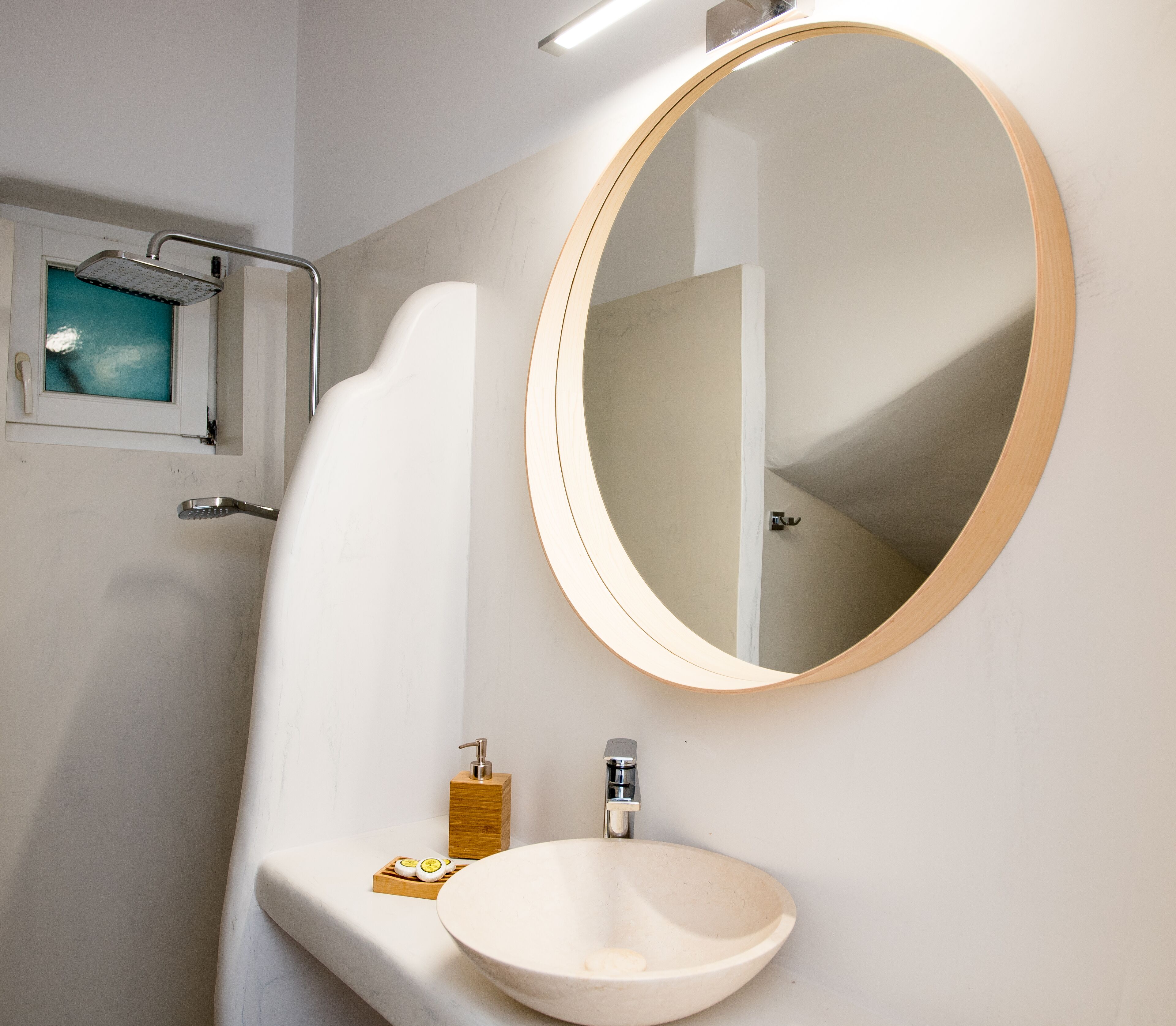 Un baño con espejo redondo, lavamanos y ducha.