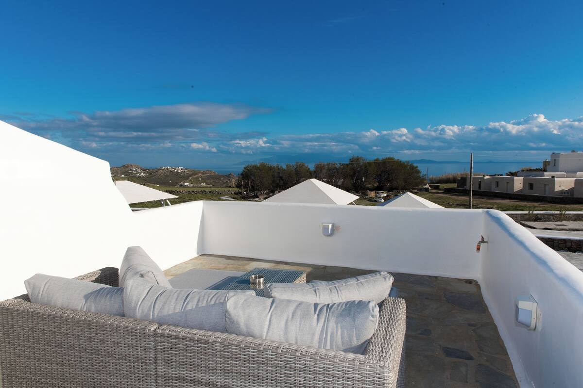 A rooftop terrace with a wicker sofa, a small table, and a view of the landscape.