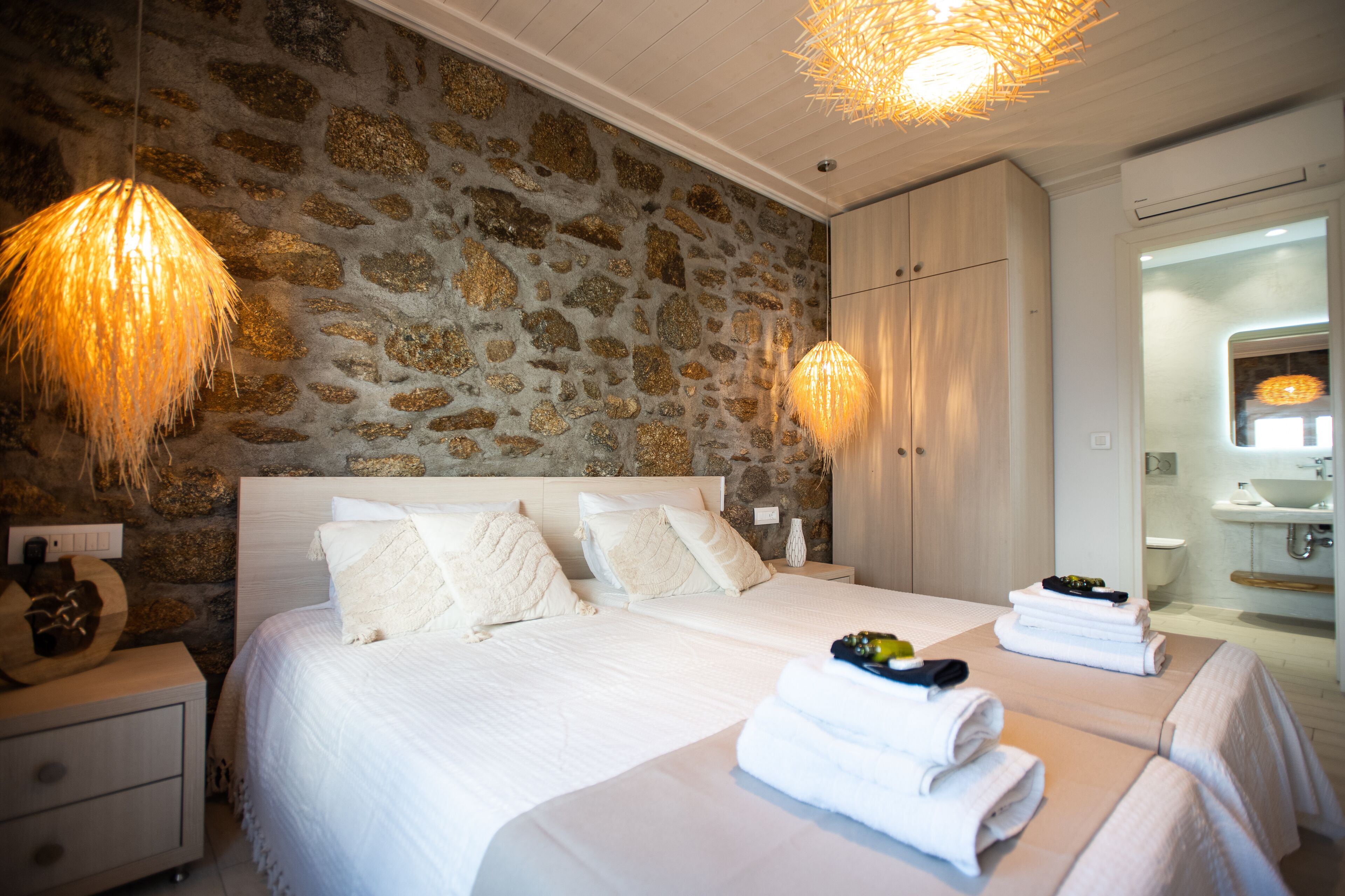 A bedroom with a stone wall, a large bed with white bedding, two bedside tables, and a modern chandelier.