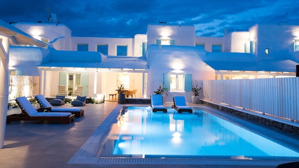 A pool area with lounge chairs and a clear pool, surrounded by white buildings with blue accents. - TIFFANYS VILLAS (Mykonos)