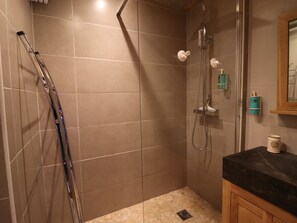 Une douche équipée d’un pommeau de douche à main, d’une porte en verre et d’un sol carrelé.
