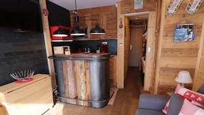 Cocina compacta con isla de madera, mesa de comedor y sofá en un espacio acogedor con paredes de madera y una pared de acento negra.