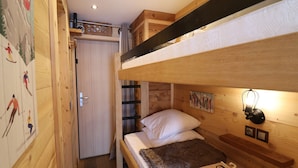 Habitación con literas, techo de madera, una puerta con cortina y un cartel temático de esquí en la pared.