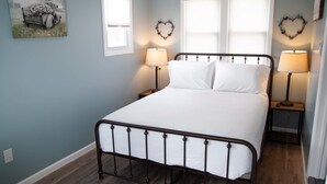 A bedroom with a metal bed frame, white bedding, two bedside lamps, and heart-shaped wall decorations.