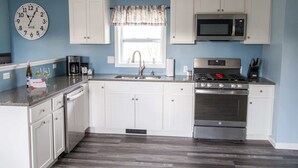 A modern kitchen with white cabinets, a stainless steel stove, a microwave, and a clock on the wall.