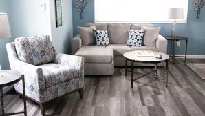 A living room with a sectional sofa, a patterned armchair, a small round table, and a lamp on a side table.