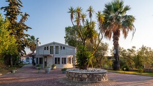 A two-story building with a paved driveway and a stone circular feature in the center. - Costa Avithos Mansion (Kefalonia)