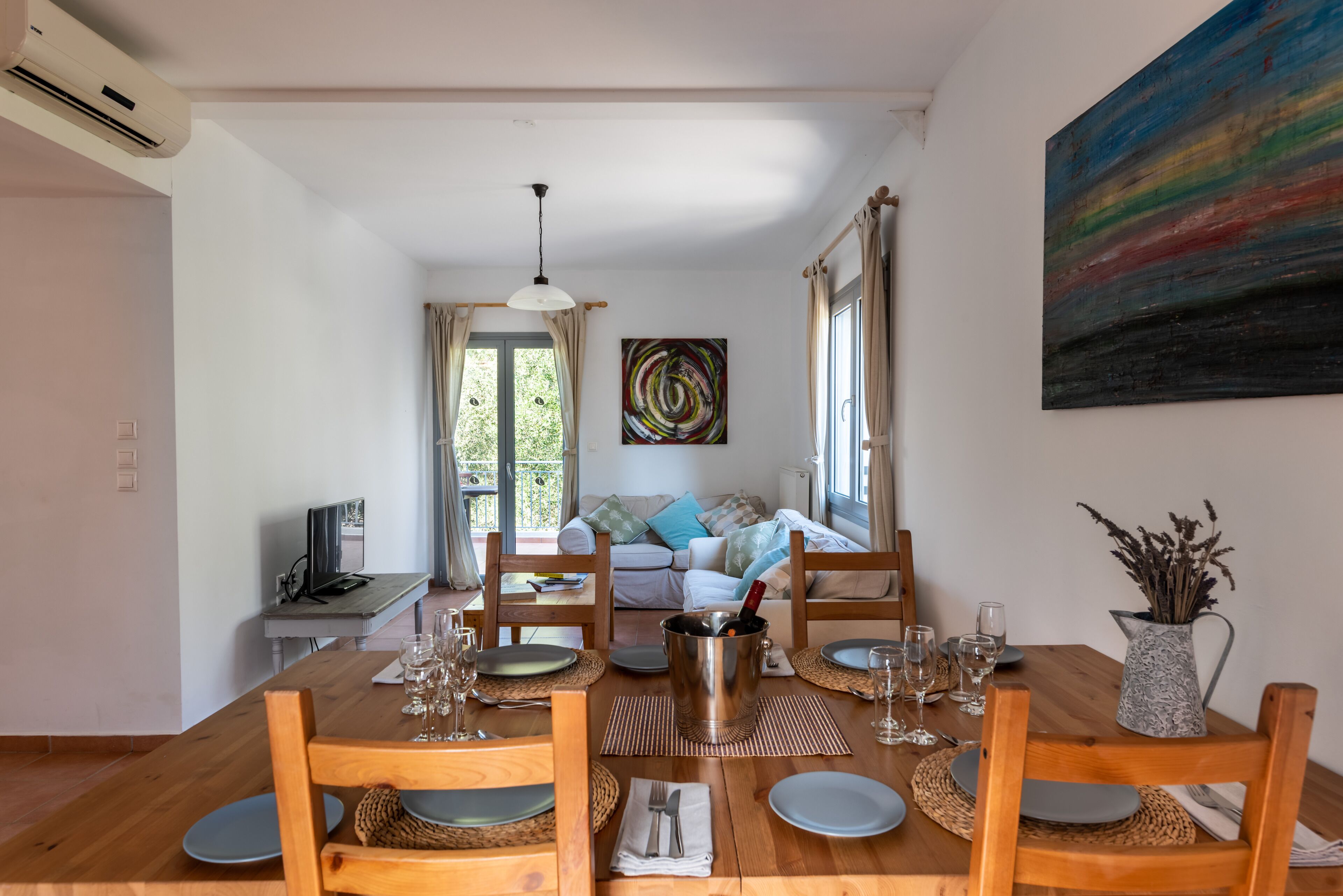 Un coin repas avec une table en bois dressée pour quatre personnes, un téléviseur et un canapé en arrière-plan.