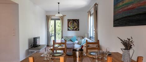 Un coin repas avec une table en bois dressée pour quatre personnes, un téléviseur et un canapé en arrière-plan.