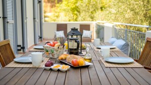 A wooden table set with breakfast items, a lantern, and a view of greenery. - Costa Avithos Mansion (Kefalonia)