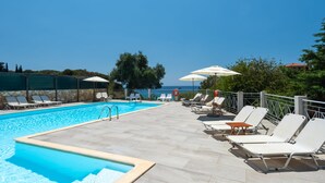 A pool area with lounge chairs and umbrellas, a clear sky, and a view of the sea. - Costa Avithos Mansion (Kefalonia)
