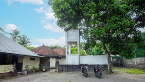 A courtyard with two motorcycles parked, a building with a tiled roof, and a large tree providing shade.