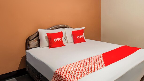 A hotel room with a bed, two pillows with the 'OYO' logo, and a patterned throw.