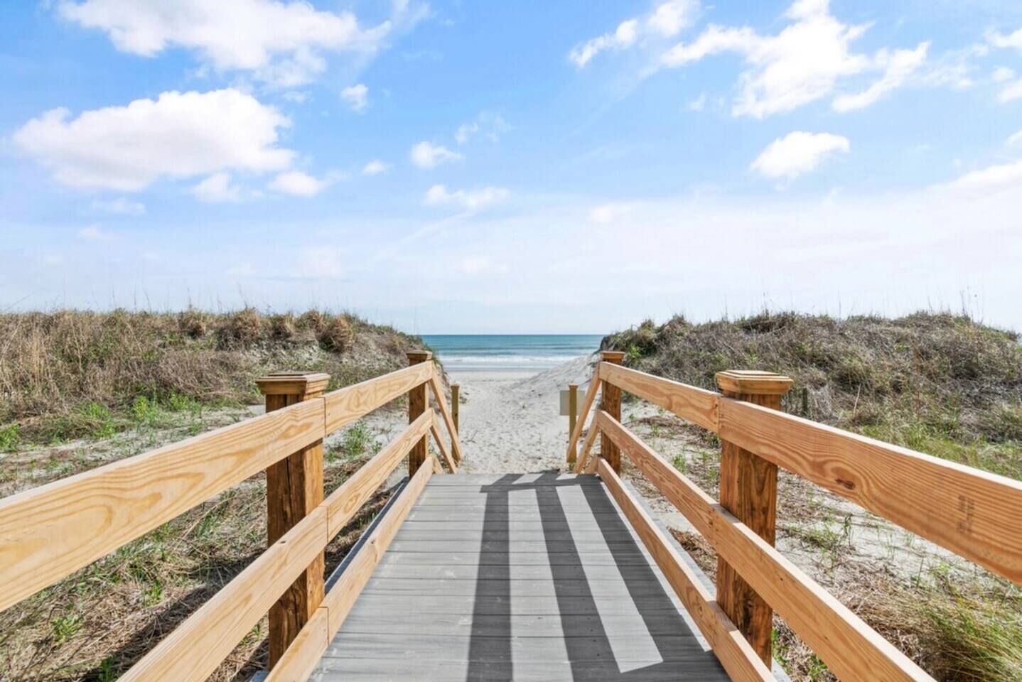 Une promenade en bois menant à une plage, avec un ciel dégagé.