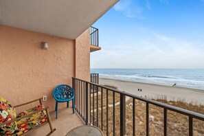 A balcony with a view of the beach, a chair, and a table. - Oceanfront at Carolina Reef w/ Pools, 2 Bds (North Myrtle Beach)