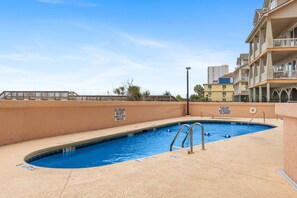 A swimming pool with a lifeguard stand, surrounded by a sandy deck and a low wall with warning signs. - Oceanfront at Carolina Reef w/ Pools, 2 Bds (North Myrtle Beach)
