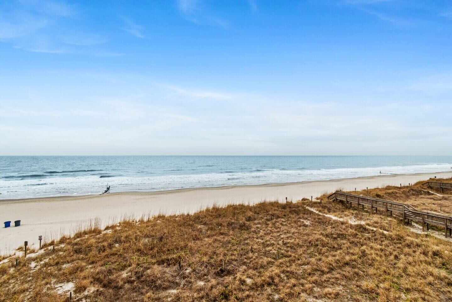 A beach with a wooden boardwalk leading to the shore, sandy dunes, and a clear sky.