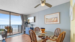 Un balcon avec vue sur l’océan, un coin repas avec des chaises et une table en osier, et un ventilateur de plafond.