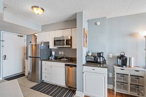 A compact kitchen with white cabinets, a stainless steel refrigerator, a microwave, a coffee maker, and a small sink. - Oceanfront at Carolina Reef w/ Pools, 2 Bds (North Myrtle Beach)