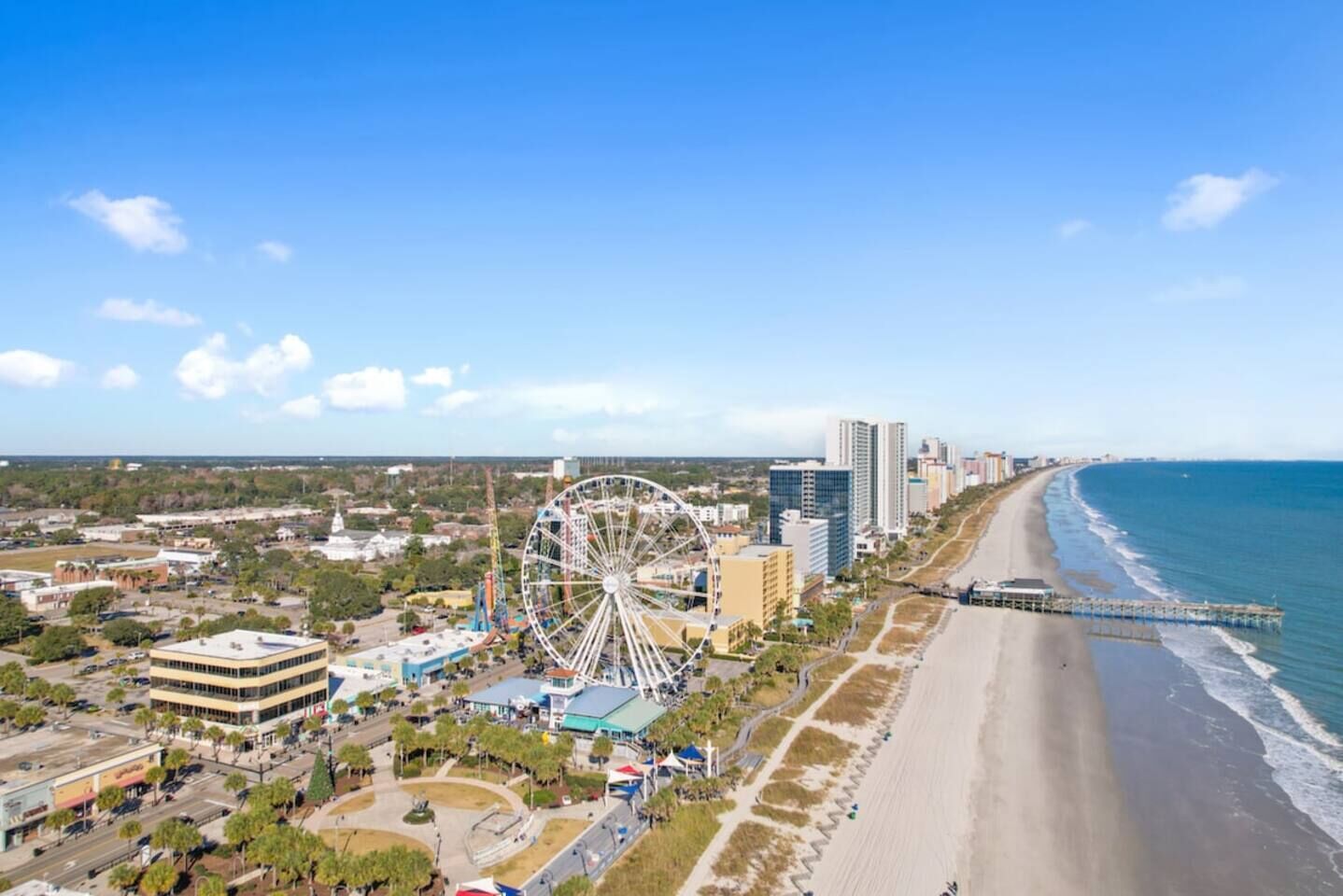 A coastal cityscape with a prominent Ferris wheel, beachfront, and high-rise buildings.