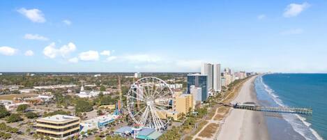 A coastal cityscape with a prominent Ferris wheel, beachfront, and high-rise buildings.
