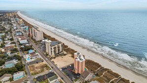 Un quartier résidentiel situé sur la côte, avec des propriétés donnant sur la plage, une route principale et un parking.