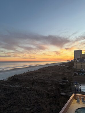 A beach view with a sunset, wooden walkways, and a pool area.