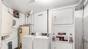 Ein kleiner Hauswirtschaftsraum mit zwei Waschmaschinen und einem Trockner, einem Warmwasserbereiter und einem Vorratsraum.