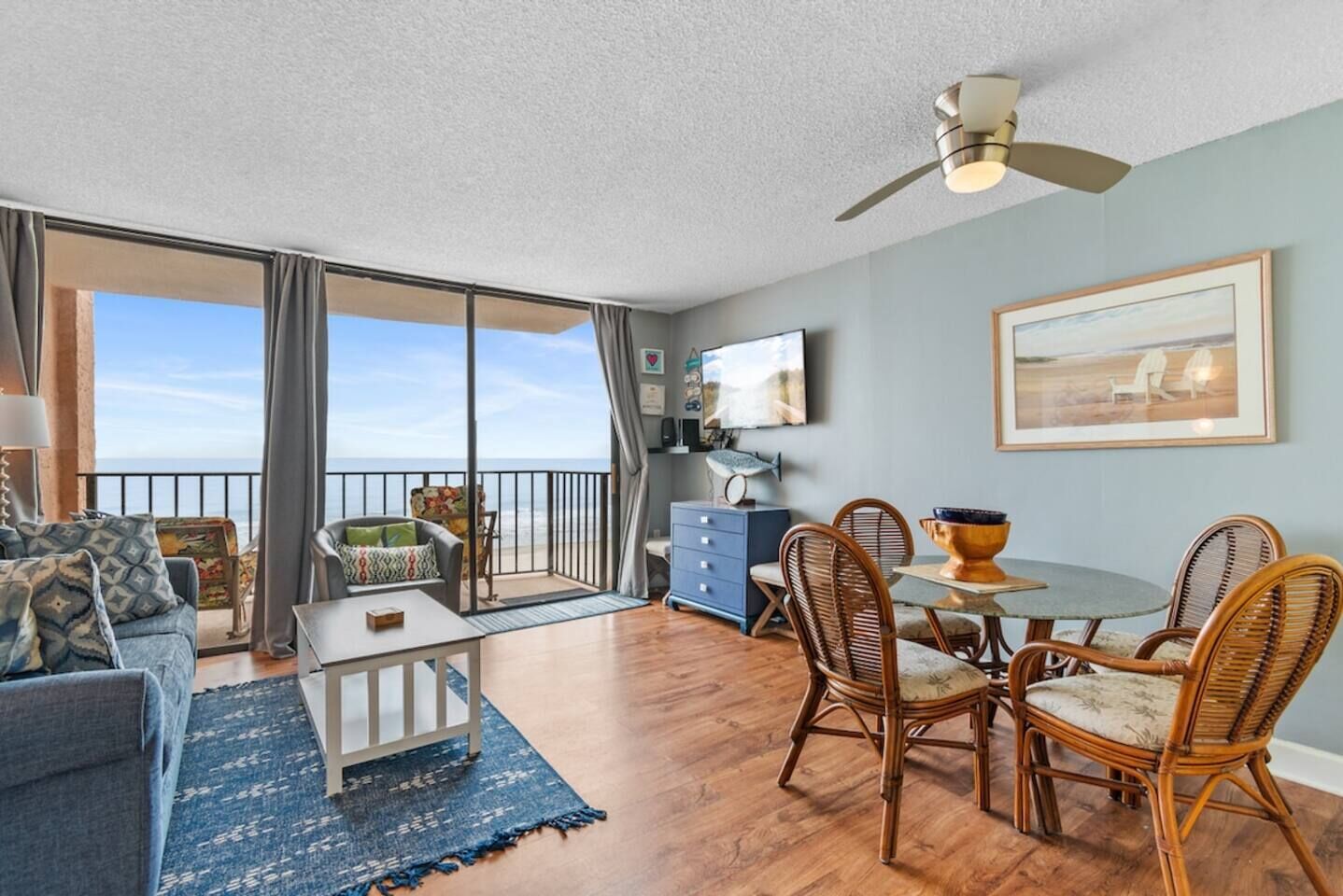 A spacious balcony with a view of the sea, furnished with a sofa, chairs, and a dining table.