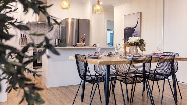 Eine moderne Küche mit einem Edelstahl-Kühlschrank, einem Holzespeisetisch und schwarzen Stühlen aus Drahtgeflecht.